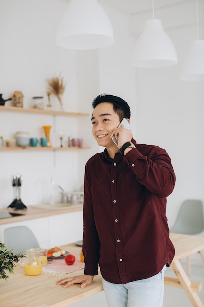 Uomo asiatico moderno che parla al telefono nella cucina a colazione.