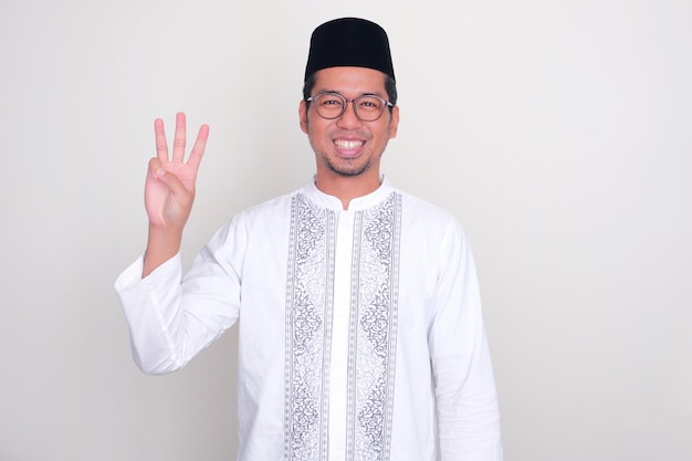Uomo asiatico musulmano che sorride alla telecamera e mostra il segno di tre dita