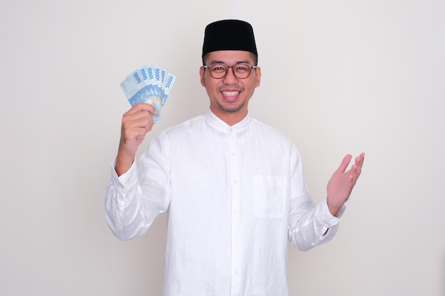 Uomo asiatico musulmano che sorride felice mentre mostra i soldi che detiene