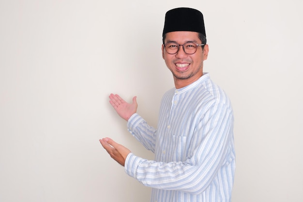 Uomo asiatico musulmano che sorride felice mentre mostra qualcosa dietro di sé