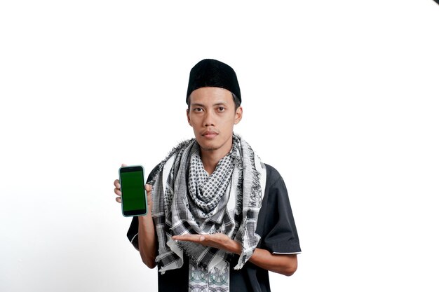 Uomo asiatico musulmano religioso che indossa abito musulmano turbante e berretto Indicando lo schermo dello smartphone sentendosi felice sorpreso o calmo isolato su sfondo bianco