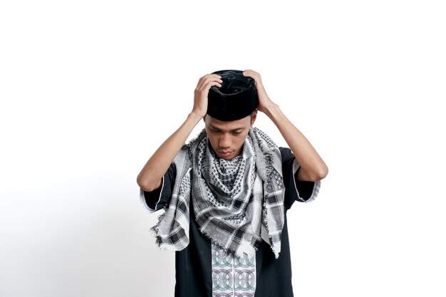Uomo asiatico musulmano religioso che indossa un abito musulmano turbante e si prepara a indossare un berretto isolato su sfondo bianco