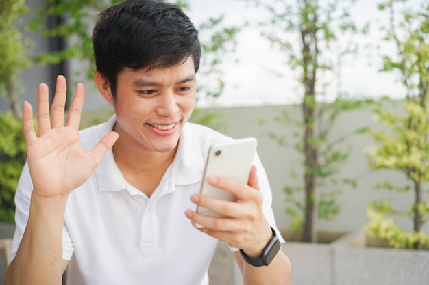 Uomo asiatico seduto al parco e utilizzando smartphone modulo di chiamata video