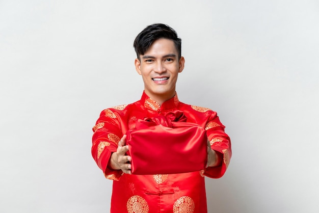 Uomo asiatico sorridente bello che fa un regalo di Capodanno cinese in uno sfondo grigio chiaro isolato