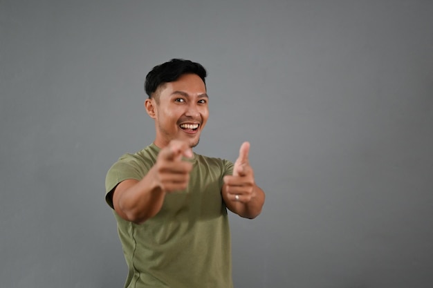 Uomo asiatico sorridente che punta il dito verso la telecamera isolata su uno sfondo grigio studio