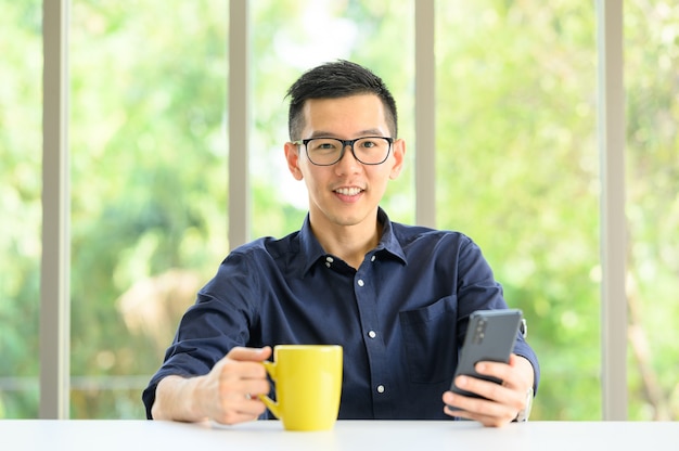 Uomo asiatico sorridente che usando il cellulare dello smartphone