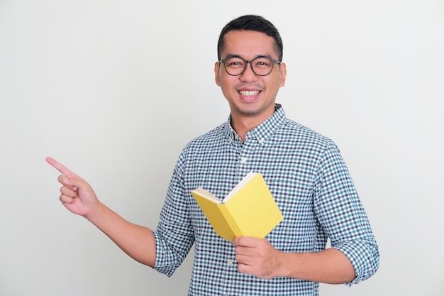 Uomo asiatico sorridente e che indica il lato destro mentre tiene un libro