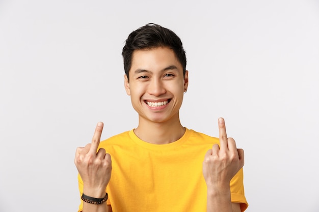 Uomo asiatico sveglio in maglietta gialla che mostra il dito medio