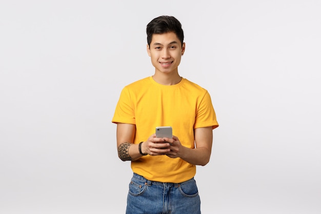 Uomo asiatico sveglio in maglietta gialla facendo uso dello smartphone