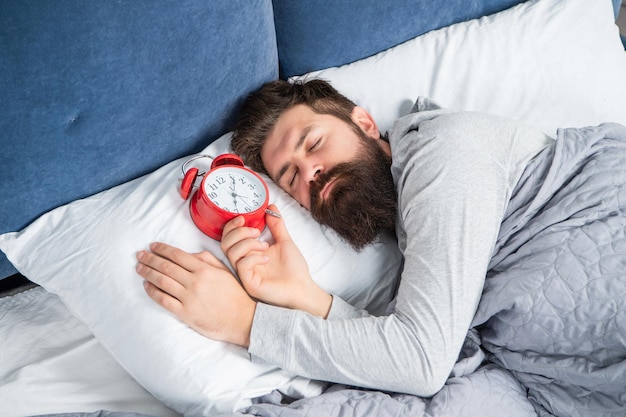 Uomo assonnato con sveglia a letto addormentato, tempo di sonno