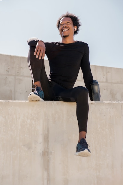 Uomo atletico afro che si distende dopo il lavoro fuori mentre è seduto all'aperto.