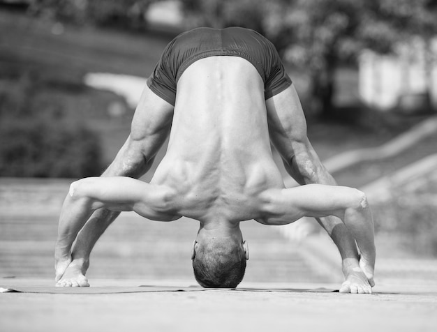 Uomo atletico bello che fa asana di yoga nel parco