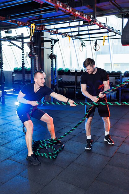 Uomo atletico che fa esercizi con l'aiuto del suo personal trainer in una palestra pubblica.