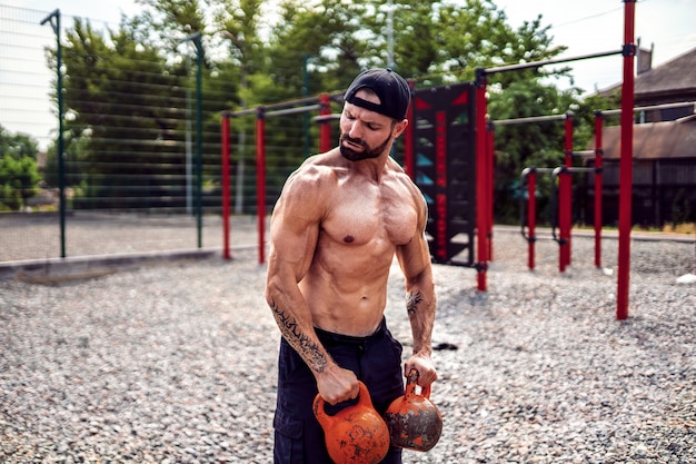 Uomo atletico che risolve con un kettlebell all'iarda della palestra della via