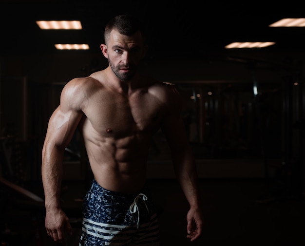 Uomo atletico con un corpo muscoloso pone in palestra, mostrando i suoi muscoli.