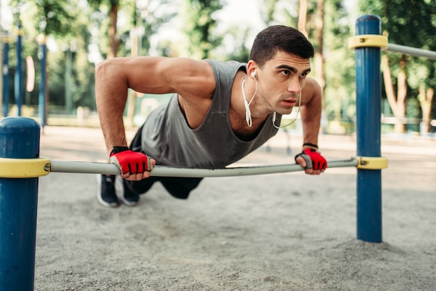 Uomo atletico facendo esercizio push-up utilizzando la barra orizzontale, allenamento fitness all'aperto. Forte sportivo sulla formazione sportiva nel parco