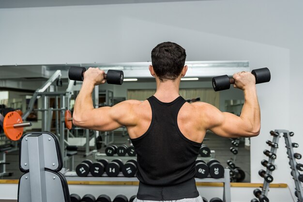 Uomo atletico in palestra lavorando con manubri