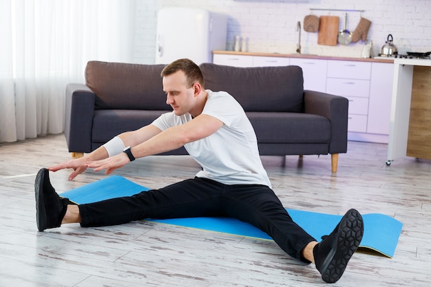 Uomo atletico muscolare in una maglietta che fa esercizi di riscaldamento a casa. Fare sport in casa durante il periodo di quarantena. Fitness fuori dalla palestra