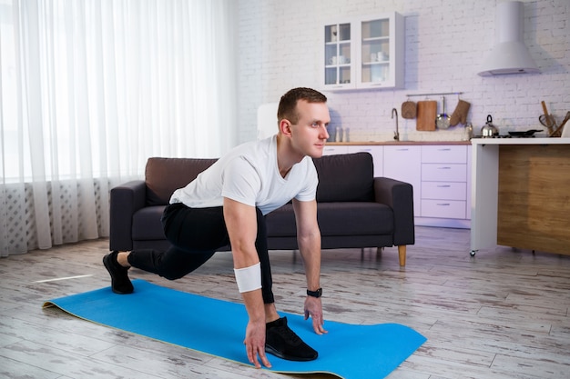 Uomo atletico muscolare in una maglietta che fa esercizi di riscaldamento a casa. Fare sport in casa durante il periodo di quarantena. Fitness fuori dalla palestra