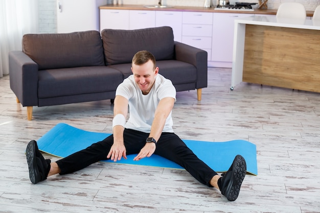 Uomo atletico muscolare in una maglietta che fa esercizi di riscaldamento a casa. Fare sport in casa durante il periodo di quarantena. Fitness fuori dalla palestra