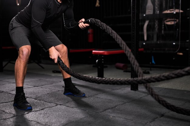 Uomo atletico ritagliata facendo esercizi di cross fit con la corda in palestra, concentrato e concentrato sulla formazione, allenamento. persone e sport, concetto di cross fit