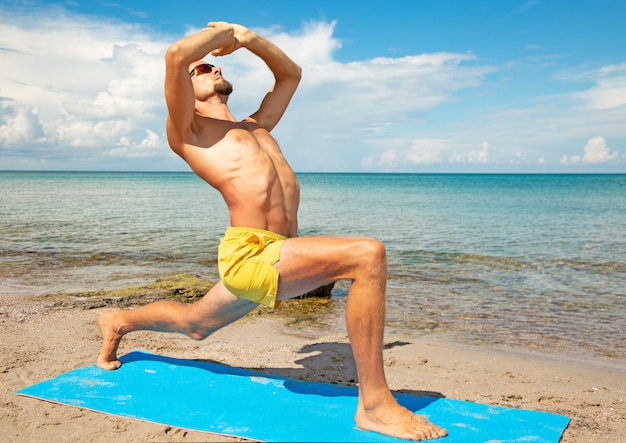 Uomo atletico sulla spiaggia che fa esercizio di yoga di forma fisica.