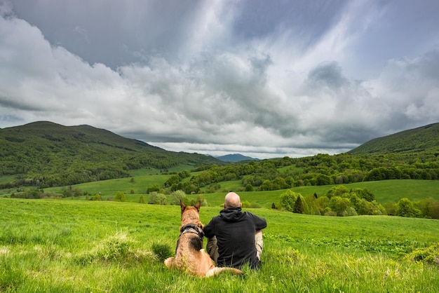 Uomo attivo seduto con il cane in montagna che guarda la visualizzazione dell'annuncio a riposo
