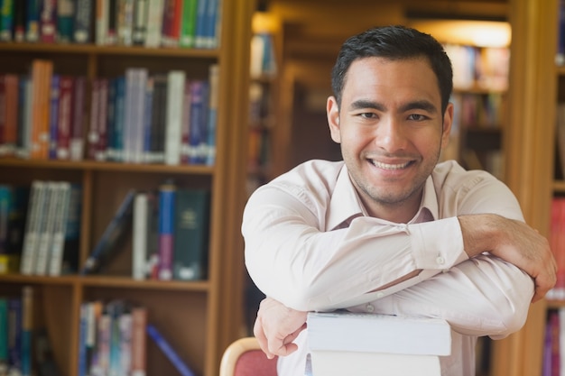 Uomo attraente allegro che posa appoggiarsi una pila di libri in biblioteca