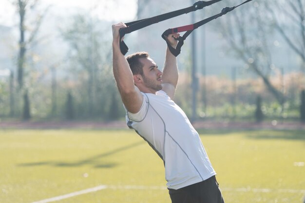 Uomo attraente che fa Crossfit con cinturini fitness Trx nell'area del parco cittadino Formazione ed esercizio fisico per il concetto di stile di vita sano di resistenza all'aperto