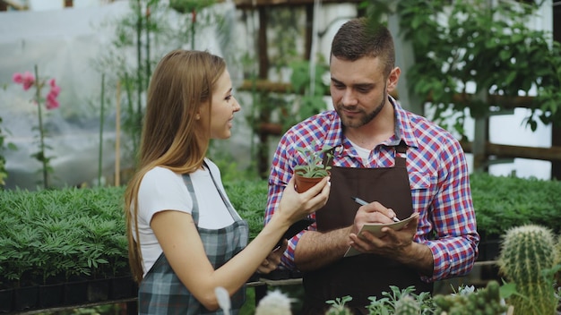 Uomo attraente cheking fiori e donna che utilizza computer tablet durante il lavoro in serra