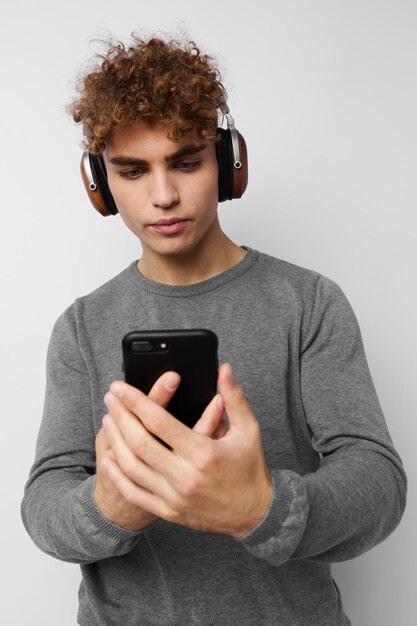 Uomo attraente con un telefono in mano che ascolta musica in cuffia sfondo chiaro