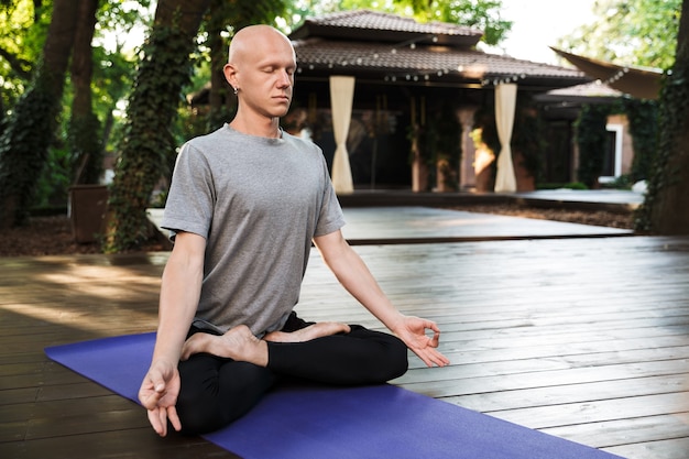 Uomo attraente di yoga fitness concentrato che medita mentre è seduto su un tappetino fitness all'aperto, gli occhi chiusi
