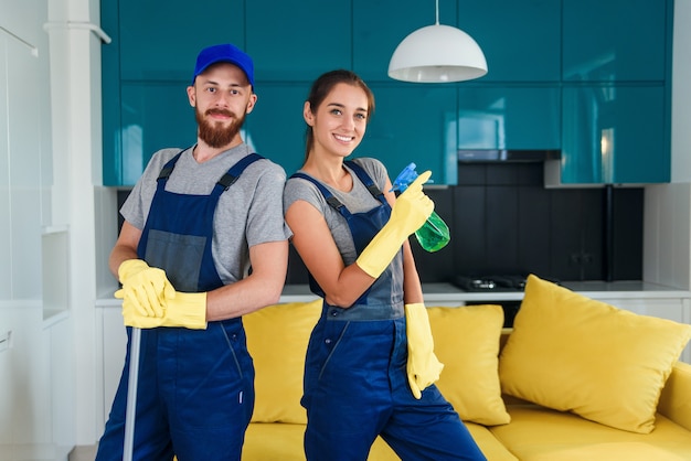 Uomo attraente e bella donna in abiti da lavoro in posa sulla macchina fotografica nella cucina contemporanea con detergenti