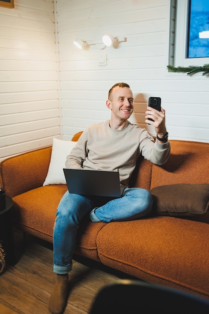 Uomo attraente seduto sul divano a casa che lavora sul portatile freelance online stile di vita moderno