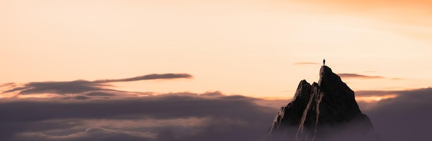 Uomo avventuroso escursionista in piedi sulla cima di una montagna rocciosa che domina il paesaggio drammatico al tramonto