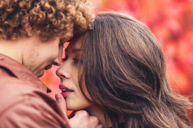 Uomo baffuto dai capelli ricci e donna dai capelli castani che abbraccia in autunno contro degli alberi rossi