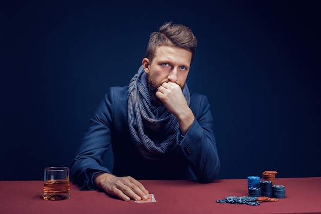 Uomo barbuto alla moda che gioca nel casinò scuro e beve whisky