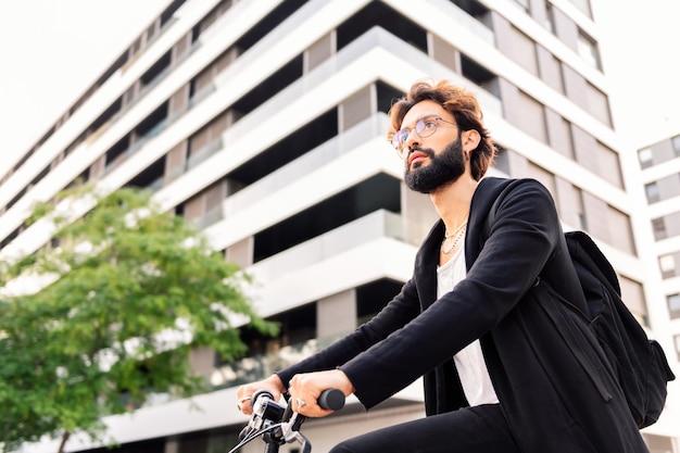 Uomo barbuto alla moda che guida una bicicletta attraverso la città