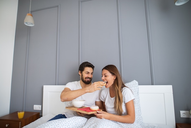 Uomo barbuto allegro che dà una bella ragazza un po 'di colazione a letto.