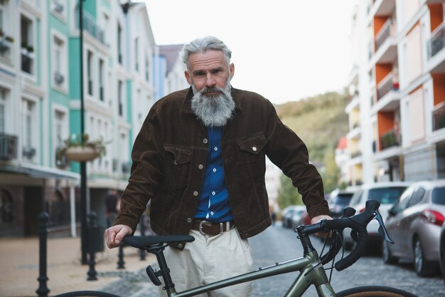 Uomo barbuto anziano che guarda con fiducia in posa con la sua bicicletta