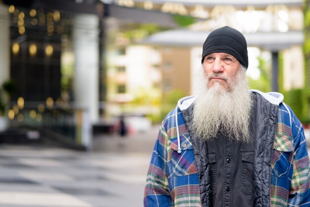 Uomo barbuto bello maturo che pensa nelle strade della città all'aperto