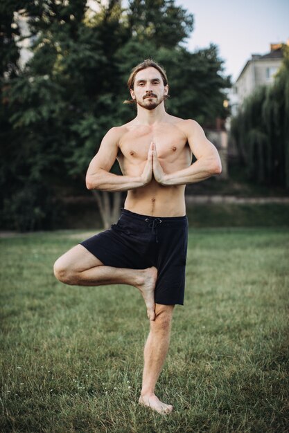 Uomo barbuto che fa yoga nel parco verde