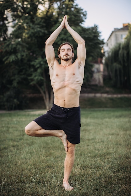 Uomo barbuto che fa yoga nel parco verde