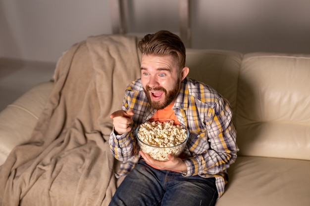 Uomo barbuto che guarda film o giochi sportivi TV mangiare popcorn in casa di notte. Cinema, campionato