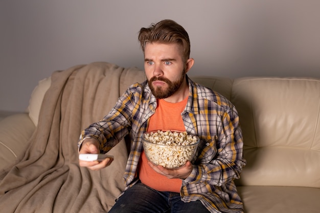 Uomo barbuto che guarda film o giochi sportivi TV mangiare popcorn in casa di notte.