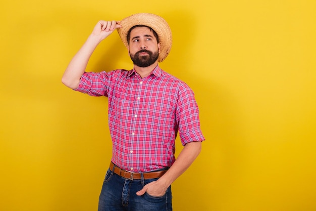 Uomo barbuto che indossa abiti tipici per la festa Junina con la mano sul cappello ottimista per la festa di Arraia