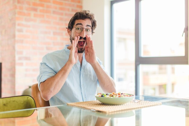 Uomo barbuto che si sente felice, eccitato e positivo, che grida con le mani vicino alla bocca, chiamando