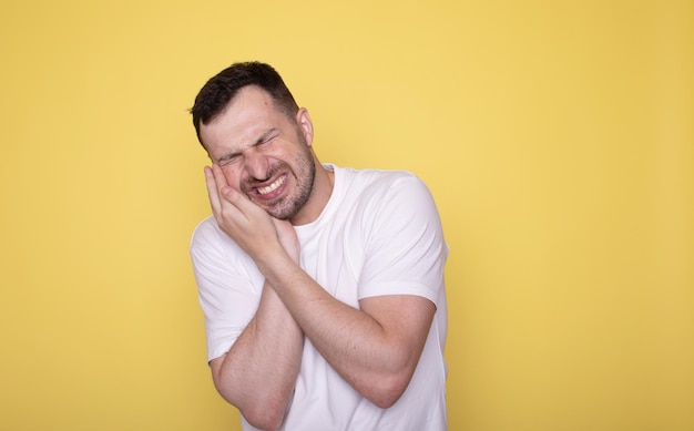 Uomo barbuto che si tocca la guancia ha mal di denti isolato su uno sfondo giallo