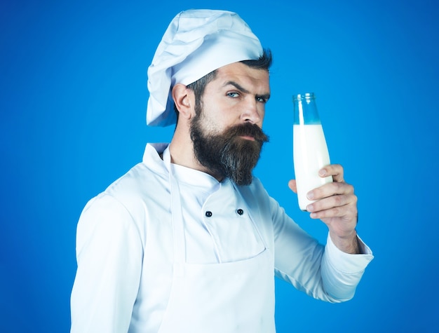 Uomo barbuto chef in uniforme con bottiglia di latte. Bevande, prodotti caseari, dieta.