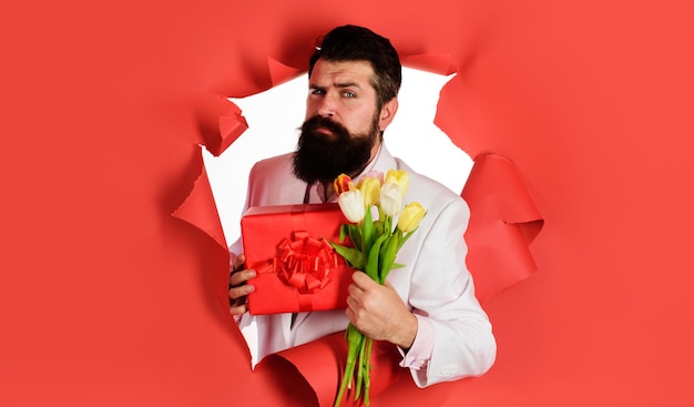 Uomo barbuto con bouquet di fiori e confezione regalo maschio romantico con regalo e tulipani San Valentino